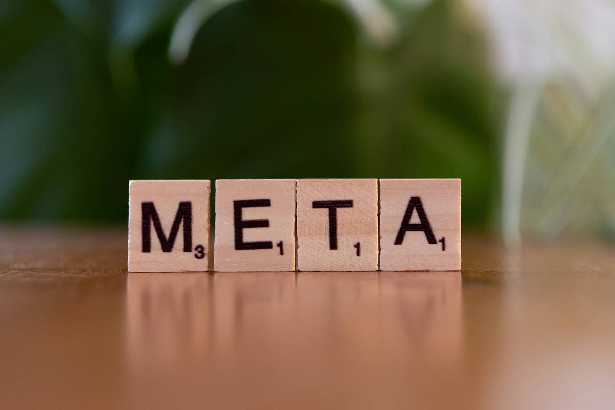 A wooden block spelling the word meta on a table